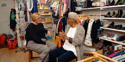 Two older women sitting in a charity shop talking