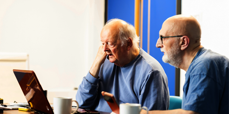 Two older men look at a laptop together