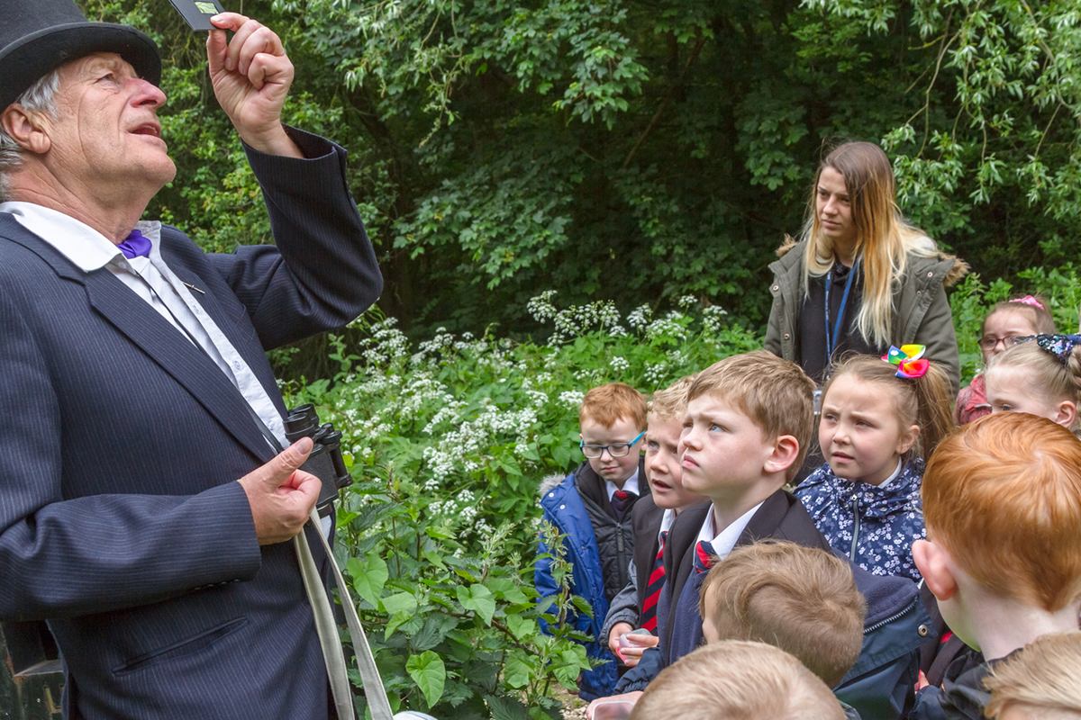 Elderly man leading a group of children in an outdoor activity.