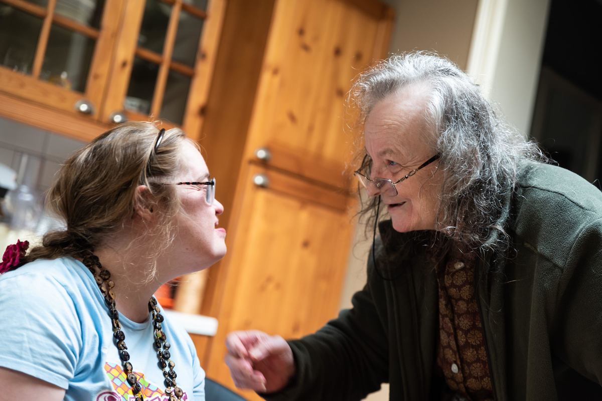 An older woman and a younger woman talk together in a kitchen