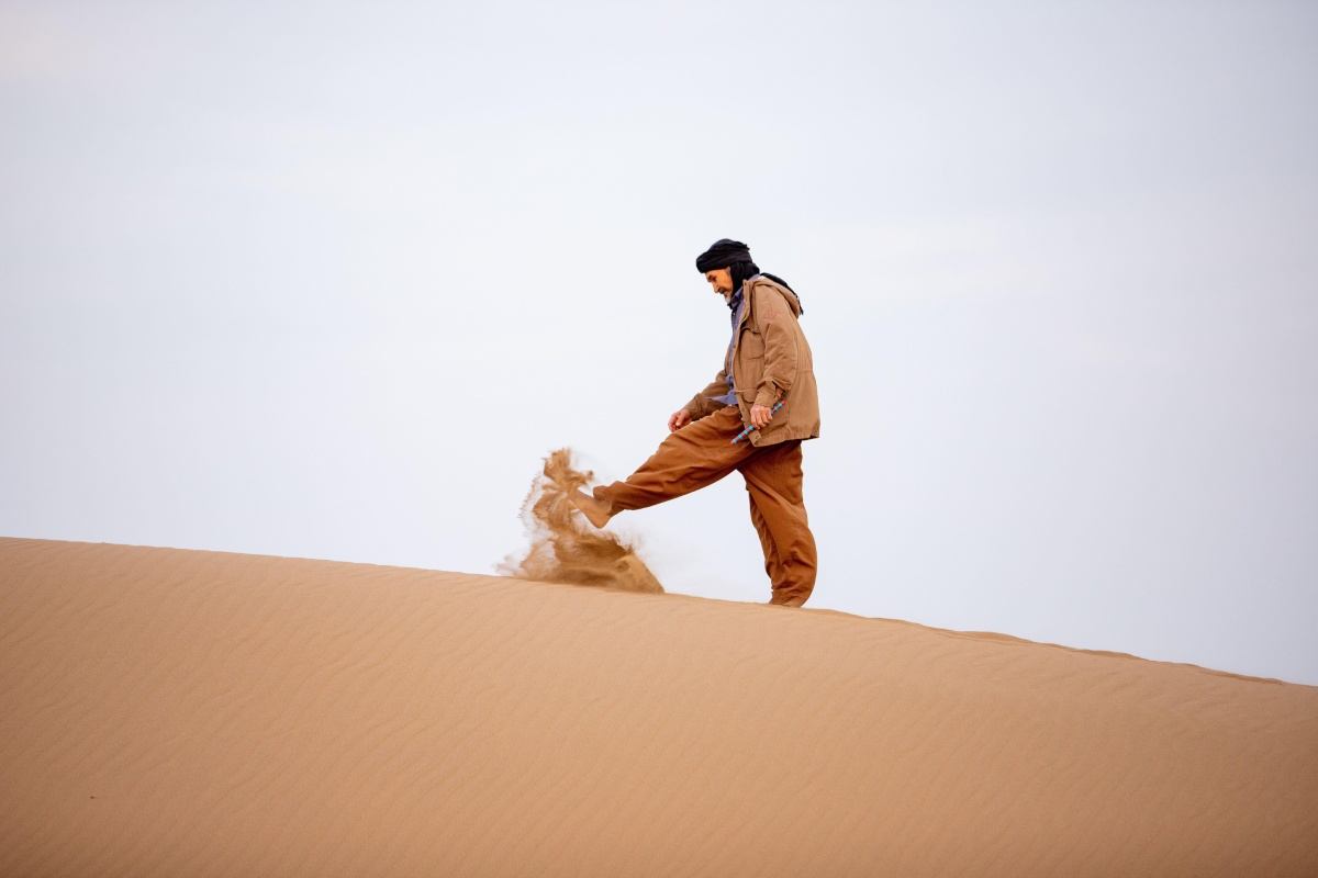 An older man on top of a sand dune kicks sand with his feet