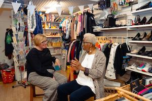 Two older women sitting in a charity shop talking