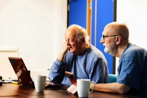 Two older men look at a laptop together