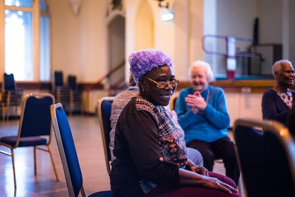 Elderly people sitting in a circle of chairs doing a gentle exercise class.