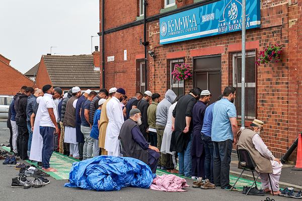 Group of muslim men prayer in front of building.