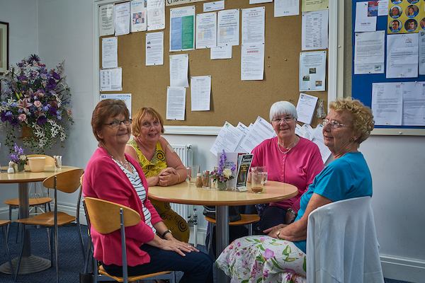 Four elderly ladies sitting around a table smiling.