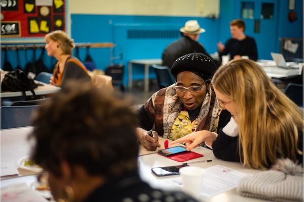 Image of a digital skills workshop: an older woman is being taught to use her smartphone by a digital skills volunteer