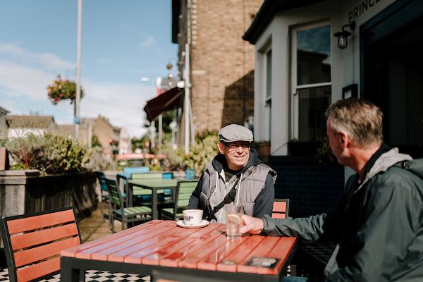 Two older men sitting by a table outside