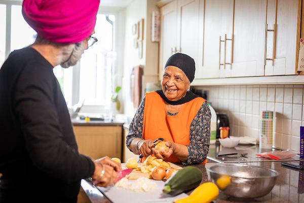 older woman chatting with a man while chopping vegetables