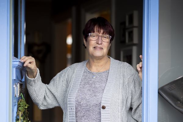 older women looking out from her front door