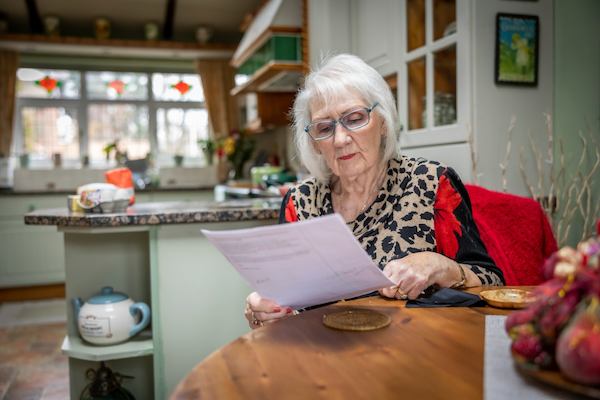 A woman wearing glasses reads a document in her home