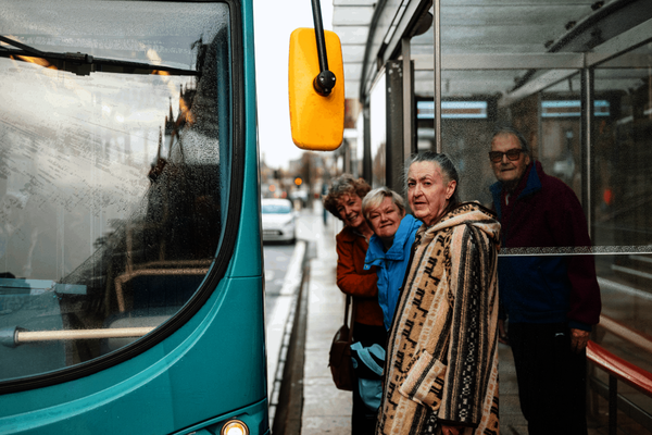 A group of older adults stand at a bus stop waiting to board the bus
