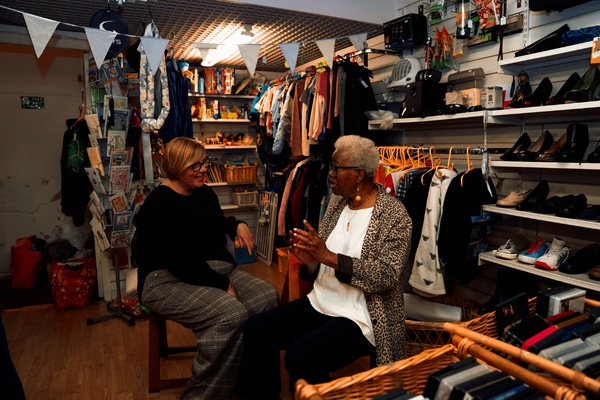 Two older women sitting in a charity shop talking