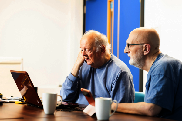 Two older men look at a laptop together